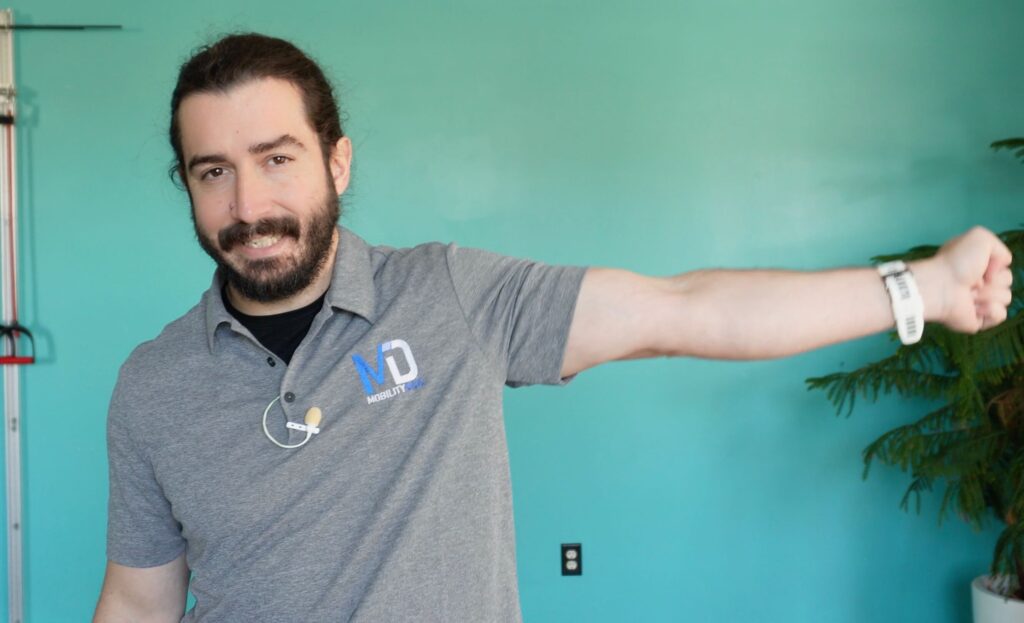 Dr. John straightening his left elbow while grimacing to demonstrate pain in the elbow while fully extended